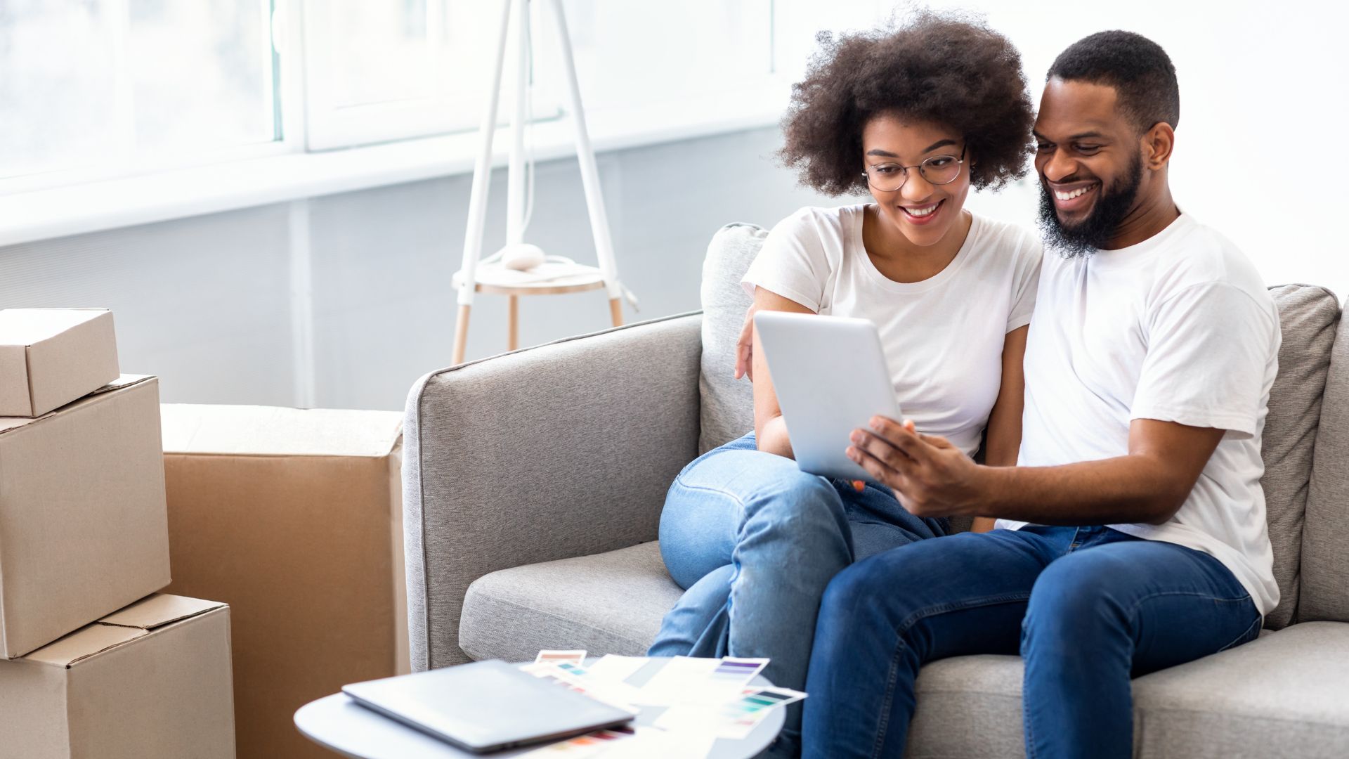 A smiling black couple sitting on a couch, using a tablet